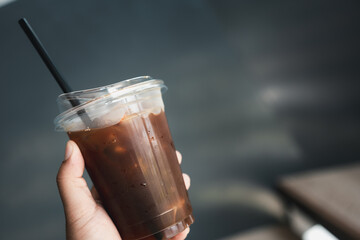 Ice black coffee in plastic cup with black straw in hand