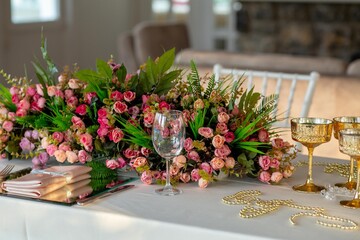 A close-up of a romantic table setting with a long floral centerpiece featuring pink roses and...
