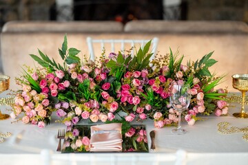 A close-up of a romantic table setting with a long floral centerpiece featuring pink roses and...