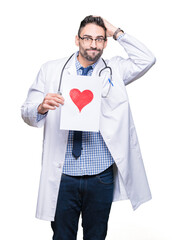 Handsome young doctor man holding paper with red heart over isolated background stressed with hand on head, shocked with shame and surprise face, angry and frustrated. Fear and upset for mistake.