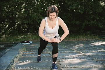 An adult woman is doing fitness in the park. The woman is doing lunges and squats.