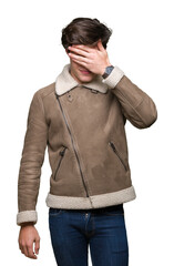 Young handsome man wearing winter coat over isolated background smiling and laughing with hand on face covering eyes for surprise. Blind concept.