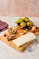 Ingredients for baked pears in dough stuffed with walnuts and honey on a wooden board on a light concrete background. Pear recipes.