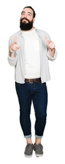 Young man with long hair, beard and earrings pointing fingers to camera with happy and funny face. Good energy and vibes.