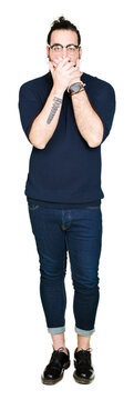 Young hipster man with long hair and beard wearing glasses shocked covering mouth with hands for mistake. Secret concept.