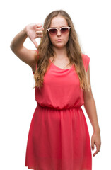 Naklejka premium Young blonde woman wearing pink sunglasses with angry face, negative sign showing dislike with thumbs down, rejection concept