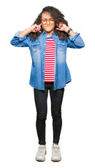 Fototapeta premium Young beautiful woman with curly hair wearing glasses covering ears with fingers with annoyed expression for the noise of loud music. Deaf concept.