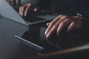 Man using digital tablet and working on laptop computer on office table. Casual business man touching on tablet screen, surfing the internet, online job, freelnace at work, close up