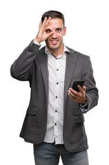 Handsome young man using smartphone with happy face smiling doing ok sign with hand on eye looking through fingers