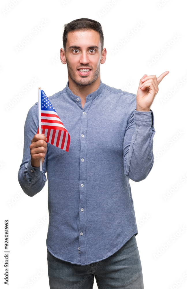 Poster handsome young man holding a flag of america very happy pointing with hand and finger to the side