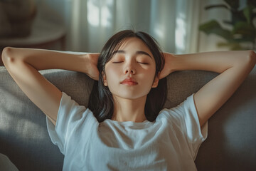 Fototapeta premium Young Asian woman unwinding on a home sofa, eyes closed and hands behind her head, dressed in casual attire, in a softly lit living room, portrayed in a hyper-realistic photorealistic style.