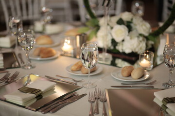 A close-up of a wedding table setting with white flowers, candles, and mirrored placemats. The table is set for a formal dinner