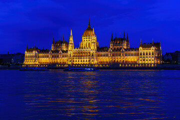Fototapeta premium Hungarian Parliament Building Illuminated at Night with River Cruises