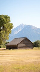 Fototapeta premium The majestic Mountains rise in the background beside an old barn and rustic fence against a bright blue sky