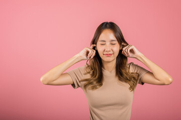 Woman bad mood pain her closed ears with finger and close eyes, Asian beautiful young female covers ears for loud noise, studio shot isolated on pink background with copy space, bad pressure