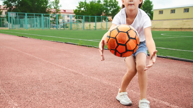 Cute child girl playing on sports ground with soccer ball outdoors