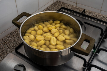 A pan of gnocchi simmering over a flame on a stovetop in a traditional restaurant kitchen, with golden pieces gently cooking in the rustic setting.