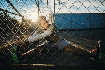 Active young man stretching outdoors in fenced area during sunset