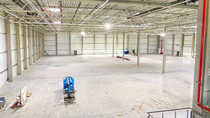 An empty warehouse with a high ceiling and concrete pillars. There are no people in the image.