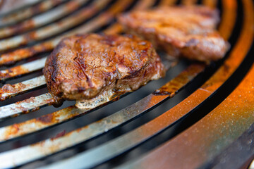 Juicy, seasoned meat steaks sizzle on a grill grate over burning coals, with flames and smoke rising as they cook to perfection.
