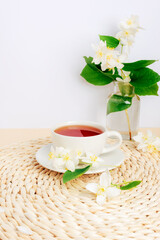 A cup of jasmine tea on a wicker place mat and jasmine flowers. Closeup