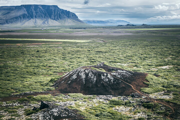 Schwarzer Vulkankrater auf weiter Ebene und Tafelberge im Hintergrund an einem sonningen Tag © Kleger photography