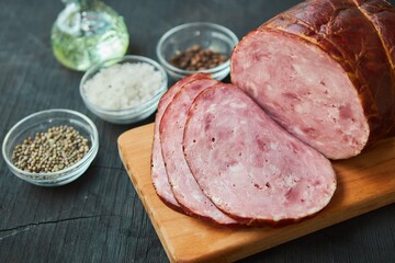 The ham lies on a wooden surface surrounded by spices. Meat production.