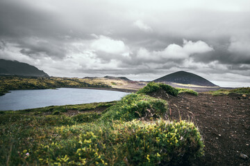 Serene Icelandic lake surrounded by rolling hills, barren landscape, mountains and a dramatic cloudy sky