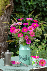 Tisch-Arrangement mit Blumenstrauß mit pink Zinnien und Gräsern, Kaffeekanne, Becher und Süßigkeiten
