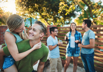 Couple, hug and party outdoor with friends, love and backyard at labor day and social event. Piggy back, conversation and happy people with summer fun, vacation and group reunion with smile and care