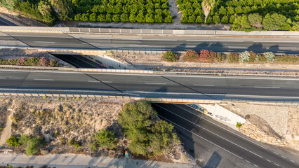 View of a highway overpass intersecting with a road in the Spanish countryside, surrounded by greenery and arid land.