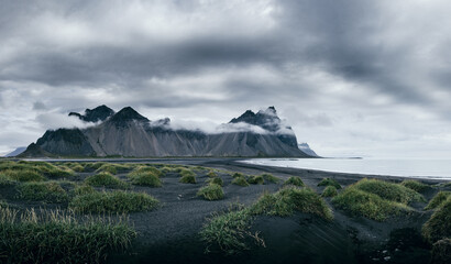 Majestätische Bergkulisse des Vestrahorn in Island unter tief hängenden Wolken, eingefangen am schwarzen Sandstrand von Stokksnes – ein raues und mystisches Landschaftspanorama mit dramatischen Kontra