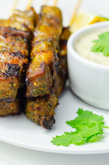 A plate of few skewers of meat with a side of sauce