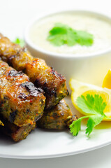 A plate of few skewers of meat with a side of sauce