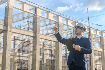 Asian adult foreman stands in front of the construction inspecting a construction project with...