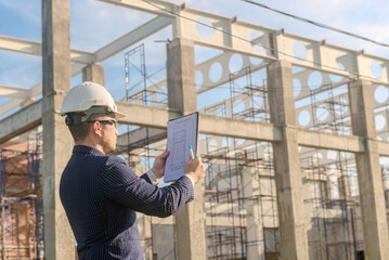 Asian adult foreman stands in front of the construction inspecting a construction project with...