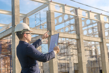 Asian adult foreman stands in front of the construction inspecting a construction project with...