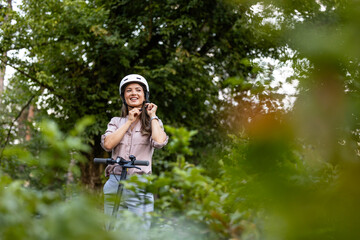 Beautiful woman putting on helmet and riding electric scooter through the park.