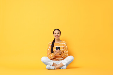 Happy woman with smartphone on yellow background