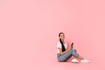 Smiling woman with smartphone on pink background. Space for text