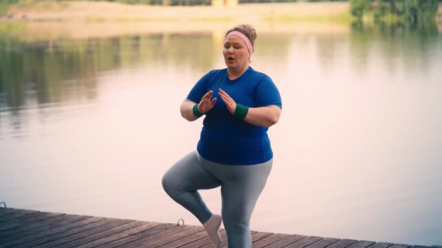 Funny plus size woman keeps losing her balance while practicing yoga outdoor
