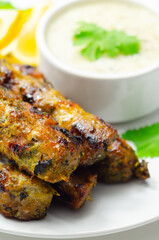 A plate of few skewers of meat with a side of sauce