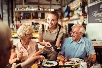 Senior friends paying for food at a bistro with a smiling waitress