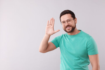 Fototapeta premium Cheerful man waving on light background. Space for text