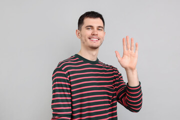 Happy young man waving on gray background