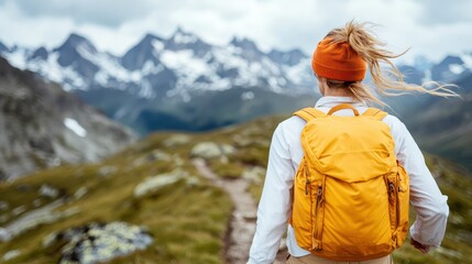 A woman with a bright orange backpack faces away from the camera, overlooking an expansive mountainous landscape. Her stance invites viewers to partake in the journey and exploration ahead.