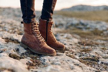 silhouetted woman in brown boots stands on rocky hillside at sunset, showcasing strong and confident stance