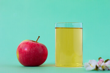 Ripe sweet red apple with a glass of fresh apple juice with apple tree flower on green background