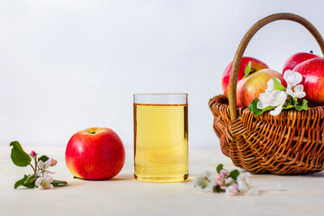 Still life, composition with sweet ripe red apple with apple fresh juice in glass with branch with flowers of apple tree. Basket with apples. Healthy vegan or vegetarian food, drink