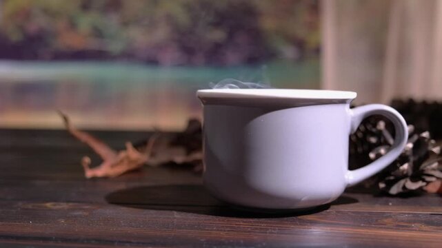 Tazza con bevanda calda fumante, rallentato, con sfondo paesaggio autunnale, foglie secche sul tavolo